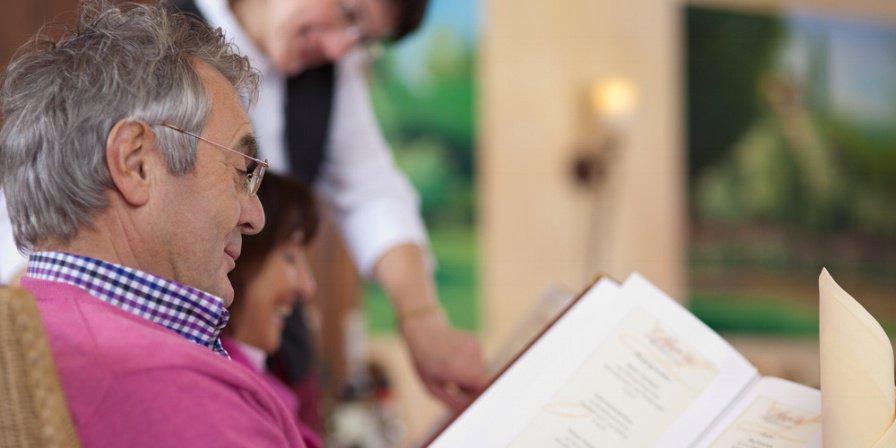 smiling guest in restaurant reading the menu with waitress in background-677453-edited.jpeg